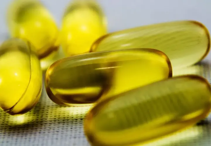 Kilka żółtych kapsułek z płynem, zawierających cenne kwasy omega 3, leży na białej powierzchni.