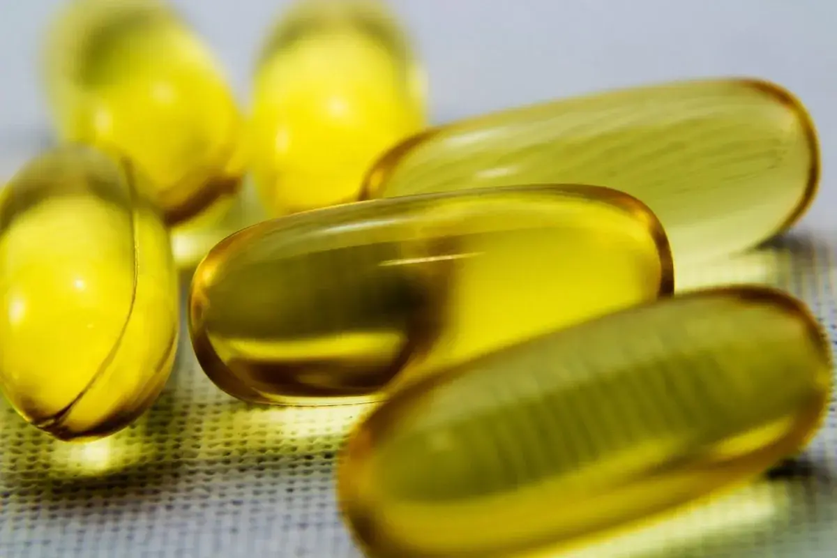 Kilka żółtych kapsułek z płynem, zawierających cenne kwasy omega 3, leży na białej powierzchni.
