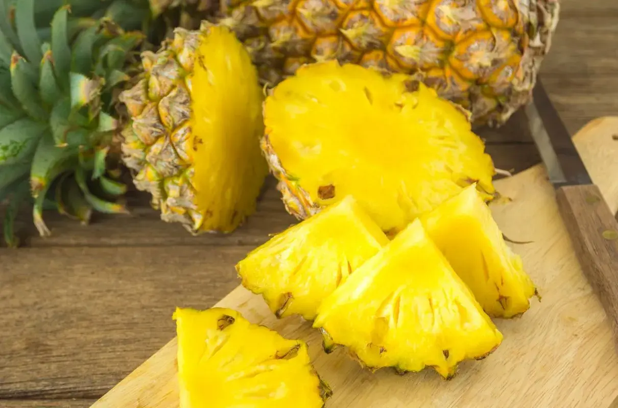 Soczyste kawałki ananasa na desce, obok całego owocu. Czy ananas jest zdrowy? Tak, to bomba witaminowa!